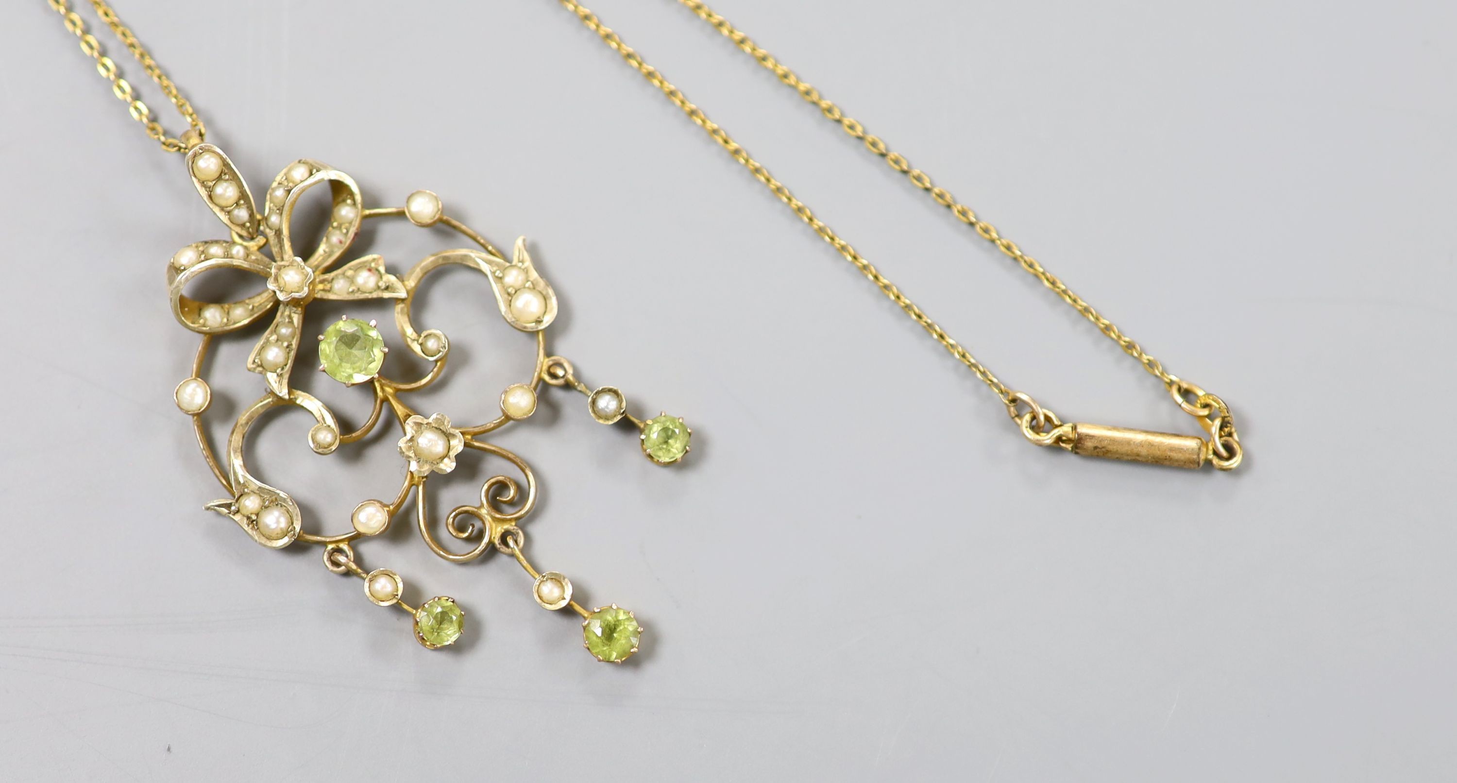 An Art Nouveau 9ct, peridot and seed pearl set scroll pendant, 46mm, gross 3.4 grams, on a gilt metal chain.
